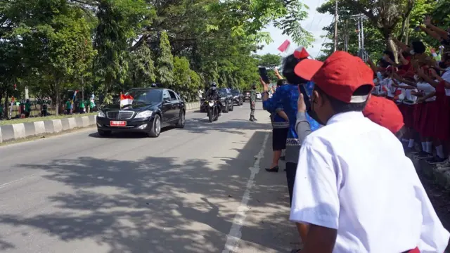 Pelajar SD mengibarkan bendera merah putih menyambut kedatangan Presiden Joko Widodo yang melintas di jalan Kota Sorong, Papua Barat, Senin (4/10/2021).