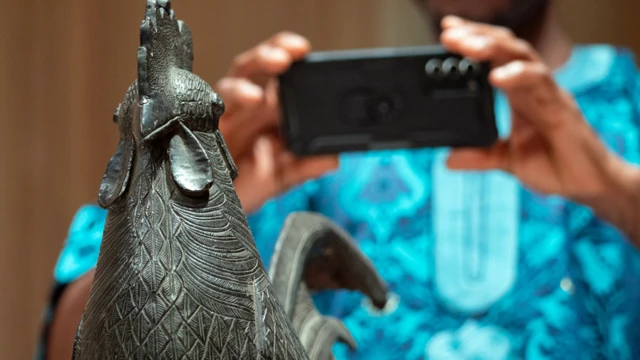 Un homme prend une photo de la statue du coq qui a été rendue au Nigeria par un collège de l'université de Cambridge