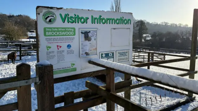 Un gran cartel dice "Información para visitantes", con la cerca y el suelo a su alrededor cubiertos de nieve.