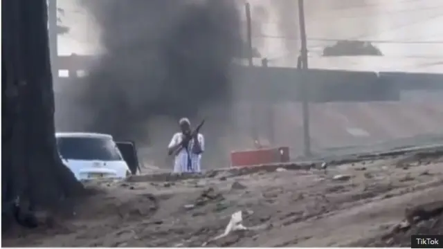 ifoto igaragara mo umugabo wambaye ishati yamabara yera afashe imbunda atunze hejuru