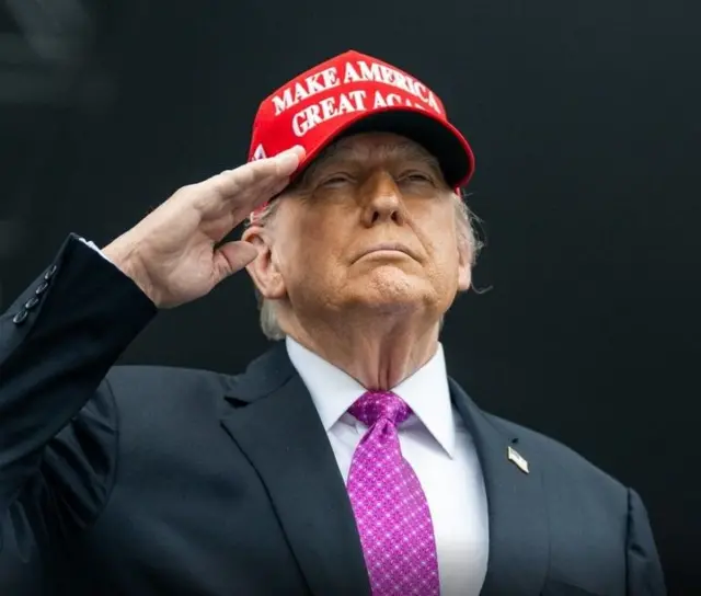 Donard Trump, Perezida wa Leta zunze ubumwe za amerika mu ikoti na Karuvati, n'ingofero yanditseho ngo ongera ugire Amerika nziza