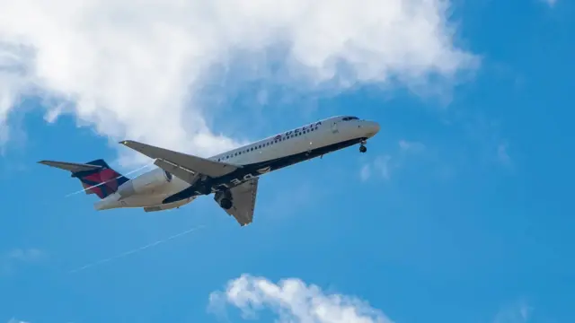 Um avião da Delta Airlines voando em céu azul, com poucas nuvens