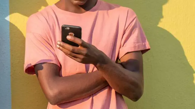 A man wit arms crossed dey look im mobile phone