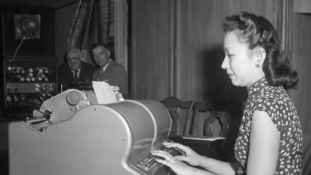 Perempuan duduk di depan mesin ketik.