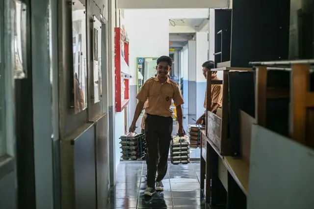 Tiga siswa membawa wadah makanan bergizi gratis (MBG) untuk dibagikan kepada teman sekelas mereka di SMA Negeri 20 di Bandung, Jawa Barat, Indonesia, pada 14 April 2025