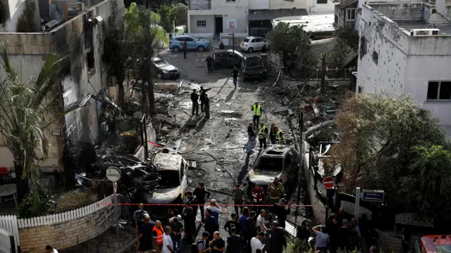 أفراد من عمال الطوارئ يعملون في موقع منازل تضررت في أعقاب هجوم صاروخي من لبنان ويقفون وسط دمار منازل وسيارات محترقة.