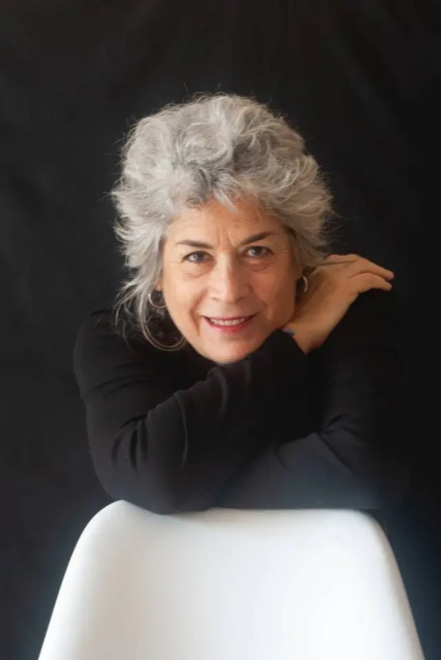 Olga Montero Rose mirando a cámara con sus brazos posándose sobre el respaldo de una silla blanca.