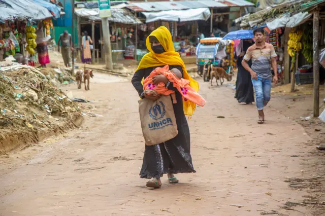 A Rohingya refugee mother with her baby walk on a road along a makeshift camp in Kutubpalang, Ukhiya Cox Bazar district, Bangladesh, 24 August 2022.