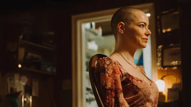 Кадр із фільму "Бугонія" - жінка з поголеною головою у сукні в профіль у кімнаті