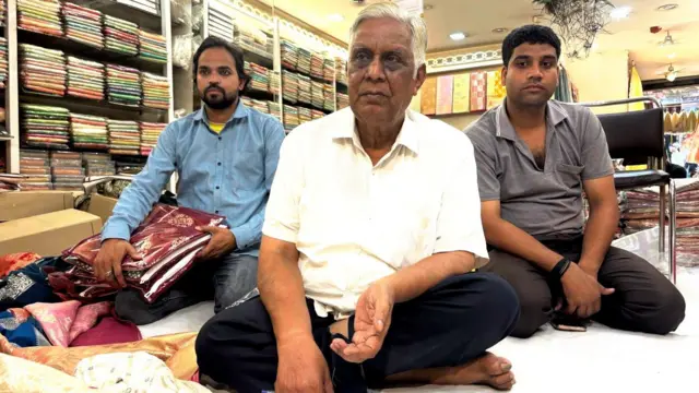 कपड़े की दुकान पर बैठे तीन व्यक्ति 