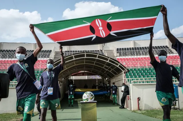 Des ramasseurs de balles masqués sortent un drapeau kényan au-dessus d'un ballon posé sur un socle au stade Nyayo de Nairobi.