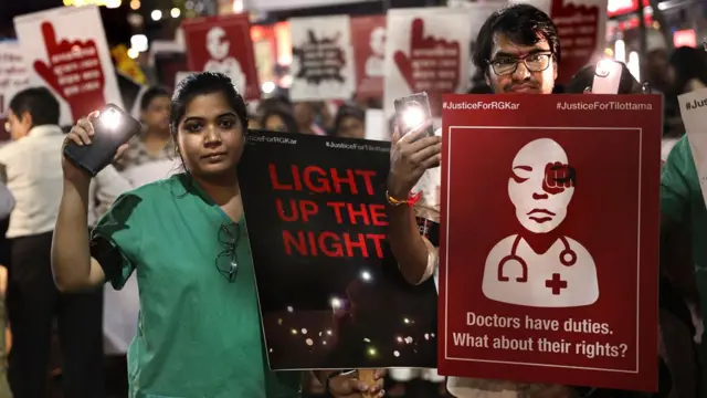 Crowds protesting in India. One person holds a banner saying: "Doctors have duties. What about their rights?" Another holds a poster saying: "Light up the night."