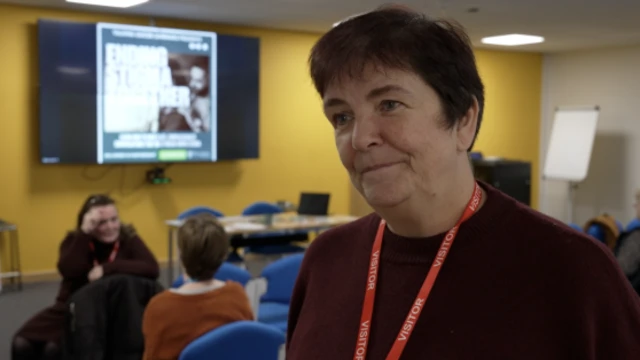 Mujer de pelo corto y oscuro que viste un jersey color burdeos y un cordón rojo para visitantes.