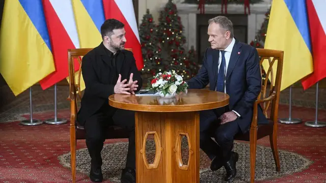 Володимир Зеленський і Дональд Туск за столом, поруч прапори Польщі і України, на задньому фоні різдвяні ялинки