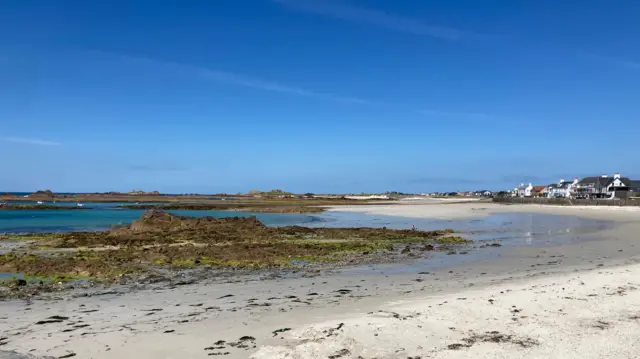 Una amplia extensión de arena conduce a un mar azul celeste en Cobo Beach en Guernsey. Es un día soleado sin nubes en el cielo.