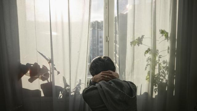 Homem com cabelos pretos é vistos bet365costas, com as mãos na nuca, olhando por uma janela