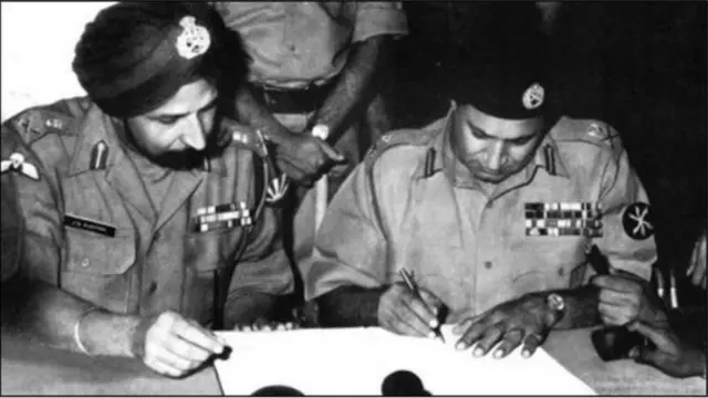 লেফটেন্যান্ট জেনারেল জগজিৎ সিং অরোরার উপস্থিতিতে আত্মসমর্পণের দলিলে স্বাক্ষর করছেন পাকিস্তানি বাহিনীর কমান্ডার লেফটেনান্ট জেনারেল নিয়াজী