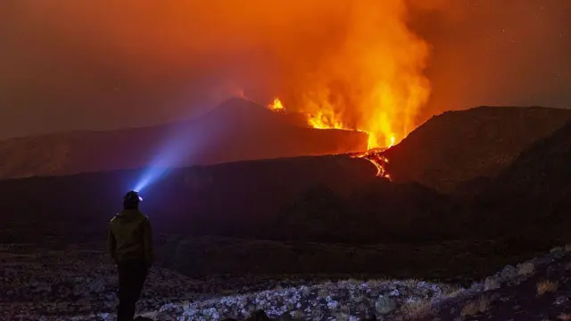 Etna Yanardağı gece lav püskürtüyor ve kafasında ışık olan biri uzaktan bakıyor. 10 Ağustos 2026.