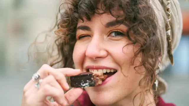 Una chica con un pañuelo en la cabeza muerde un chocolate