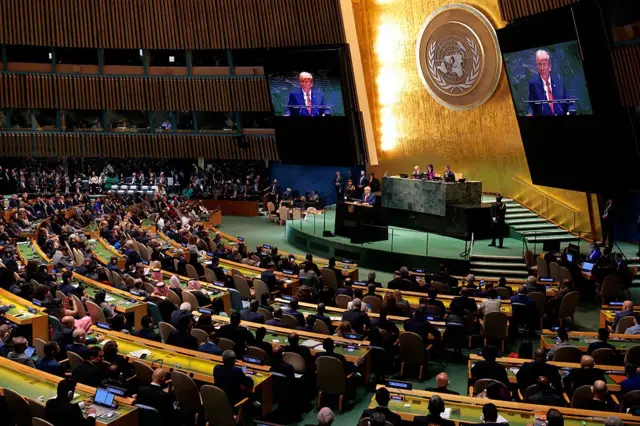 Plateia na ONU sentada. Ao fundo, Trump discursando no púlpito