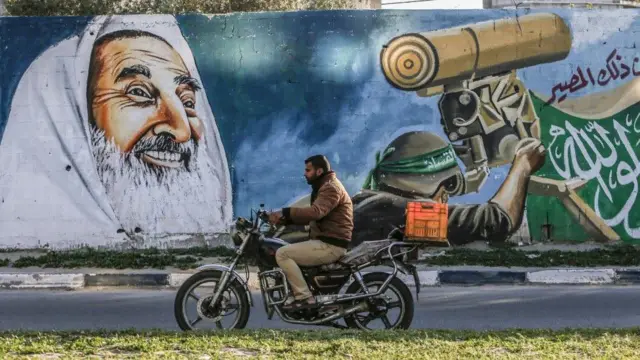 A Palestinian man drives a motorcycle past a mural depicting late Hamas spir