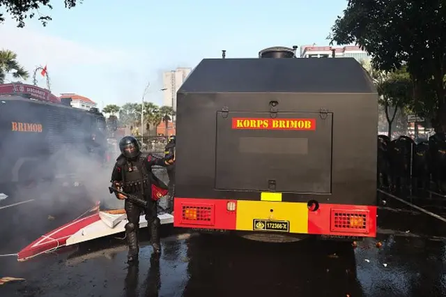 Petugas Kepolisian Indonesia bersembunyi di balik perisai selama protes terhadap Kepresidenan Prabowo pada 29 Agustus 2025 di Surabaya, Indonesia. 