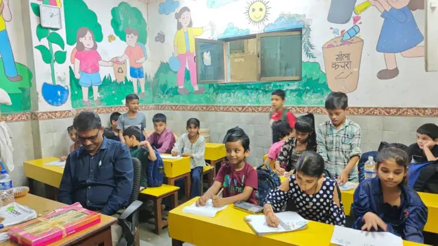 Los niños se sientan en un aula con paredes cubiertas de murales sobre la eliminación de residuos.
