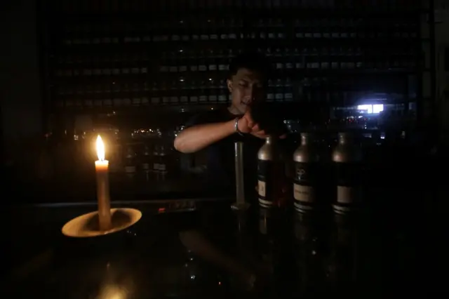 Seorang pedagang menutup botol minyak wangi dengan bantuan penerangan lilin di toko parfum.