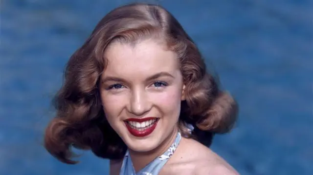 Marilyn Monroe sonríe en una imagen de 1946, tiene elcabello castaño y los labios pintados.