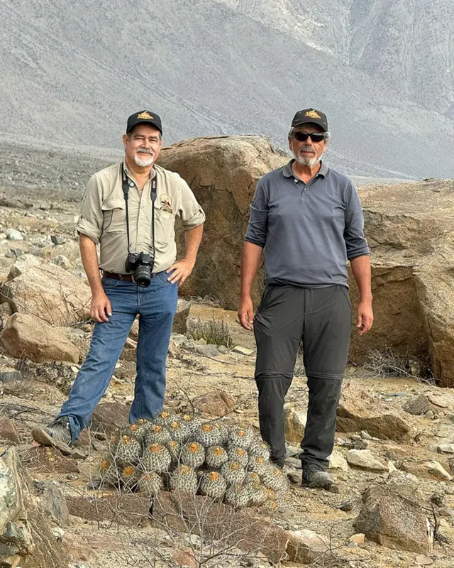 Mauricio Gonzalez y Rodrigo Castillo, ataviados con ropa de campo, en mitad del desierto con varios ejemplares de cactus a sus pies. 