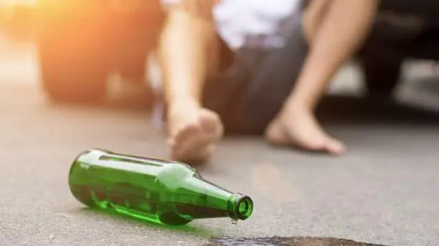 Ілюстративне фото, на першому плані порожня пляшка від алкоголю, вдалині в кріслі сидить чоловік у розслабленій позі, обличчя його не видно.