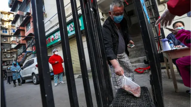 A man takes up a bag of pork as residents line up to buy pork at the gate to the closed community in Wuhan in central China's Hubei province Wednesday, March 18, 2020