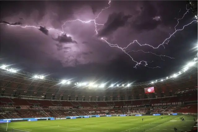 Lightning bolts are seen in a dark sky above an empty football stadium