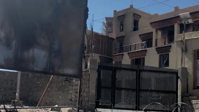 एक मकान जिसके बाहर एक बोर्ड जला हुआ है और वॉयर बिछाया हुआ है.