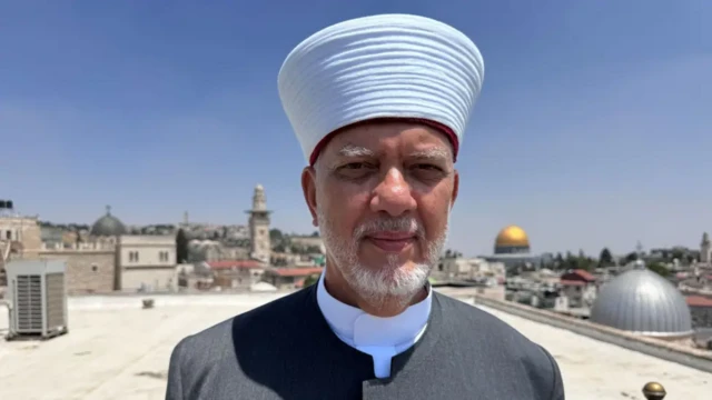نمای نزدیک از چهره دکتر مصطفی ابوسوی که بر پشت بامی ایستاده و پشت سر او نمایی از شهر و گنبد مسجد القصی دیده می‌شود