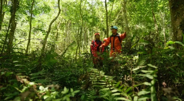 Duas pessoascasas de apostas em dolarmeio à vegetação, usando roupas vermelhas com equipamentoscasas de apostascasas de apostas em dolardolarproteção, inclusive um capacete