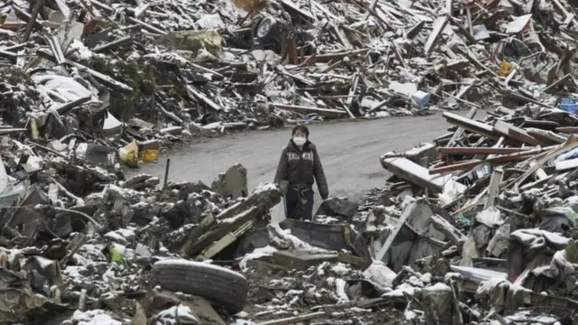 Uma mulher caminha entre os escombros na cidade japonesa de Minamisanriku, no norte do Japão, após o tsunami de 2011. 