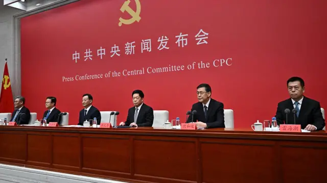 中共成员围坐在红色背景前的桌子旁。