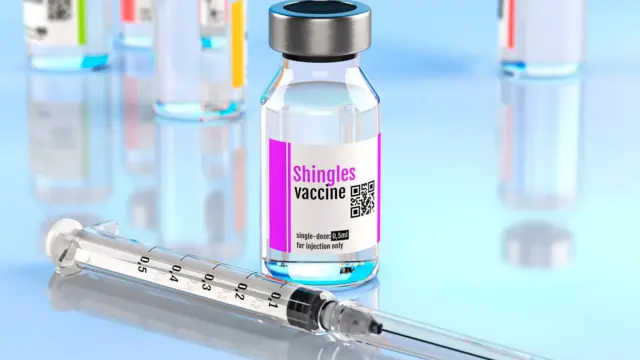 una botella con la vacuna contra hérpes zóster junto a una jeringa