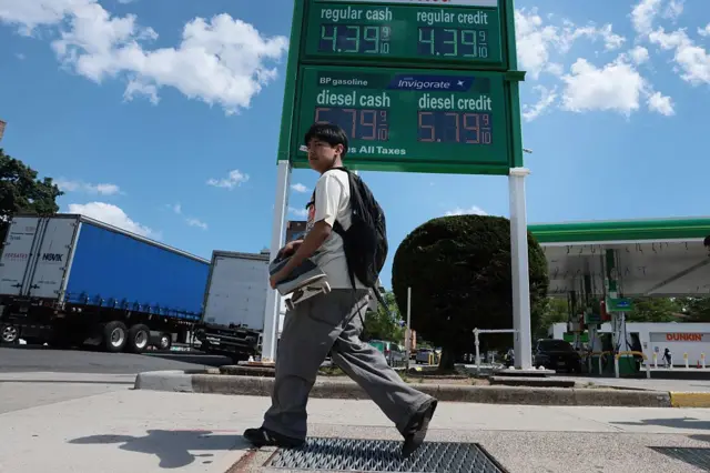 Un hombre pasa frente a una gasolinera, donde se muestran los precios por galón, en Nueva York