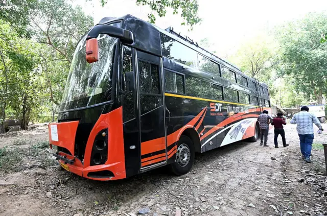 কালো ও কমলা রংয়ের একটি বাস। পাশে তিন জন ব্যক্তি হেঁটে যাচ্ছে যাদের পেছনের অংশ দেখা যাচ্ছে