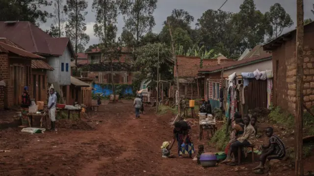 On a street in Mugole, people stand on the side of a dirt road to display their wares on the island of Idjwi, South Kivu province. The houses look rundown.