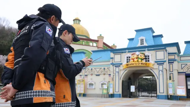 오월드 테마파크 입구 앞에서 리모컨을 들여다보는 두 명의 소방관