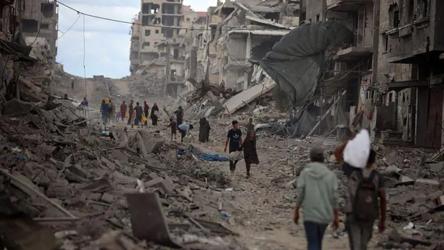 Palestinos caminan por una calle llena de escombros.