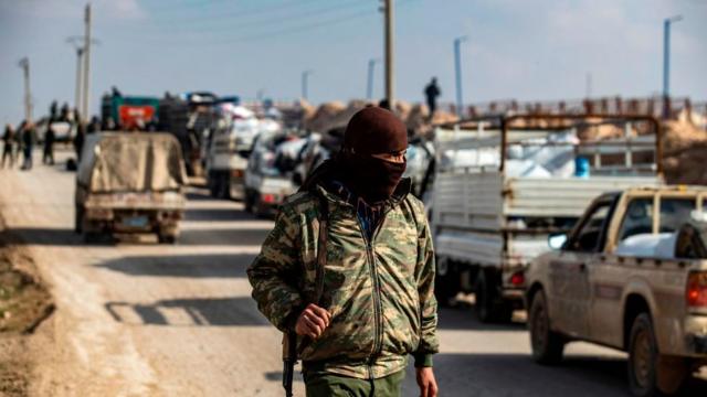 أحد عناصر دورية الأمن الداخلي يقف أمام قافلة شاحنات في مخيم الهول الذي تديره القوات الكردية، ينقل نساء وأطفال سوريين يشتبه في ارتباطهم بمقاتلي تنظيم "الدولة الإسلامية".