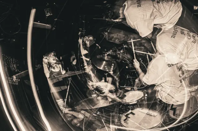 Размытая движением фотография показывает вокалиста, гитариста и барабанщика панк‑группы Sailboat в момент выступления 