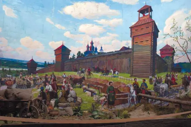 Це мальовниче історичне зображення, яке показує сцену життя біля дерев’яної фортеці. На передньому плані – жвава торгівля та рух: люди в традиційному одязі сидять і стоять біля возів, мішків і бочок, поруч коні та візки з вантажем. У центрі – дерев’яні стіни укріплення з високими вежами, а за ними видно куполи православної церкви. На задньому плані – зелений ландшафт і річка під блакитним небом із білими хмарами.