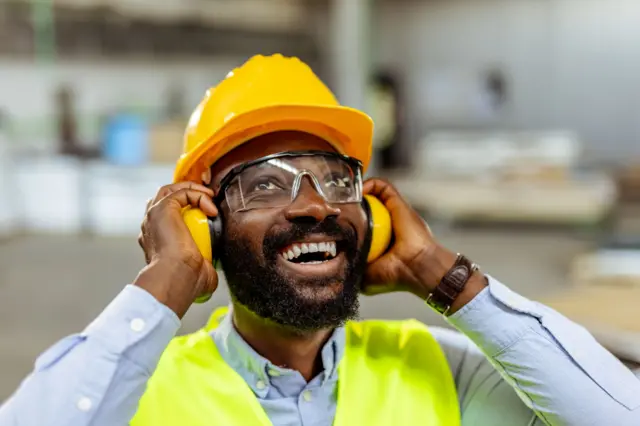 Ouvrier du bâtiment souriant et portant un équipement de sécurité à l’intérieur d’un atelier industriel