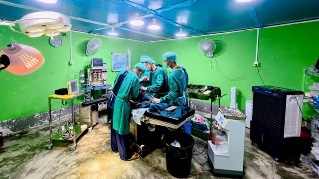 The operating theatre, with three doctors wearing green scrubs and facemasks