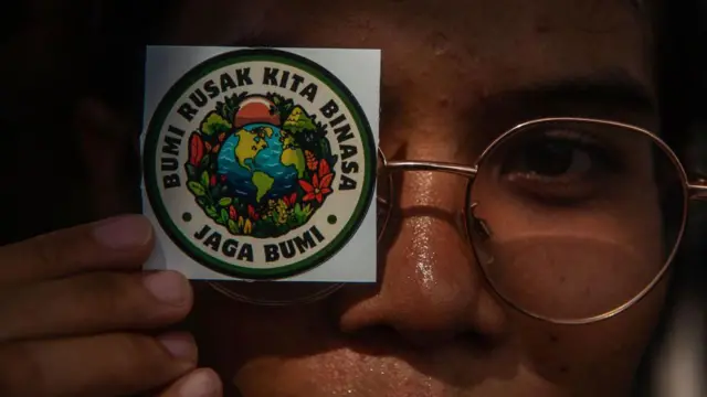 Seorang aktivis dari organisasi lingkungan Indonesia menunjukkan spanduk protes untuk memperingati Hari Bumi di sepanjang jalan pusat Kota Medan, Sumatera Utara, Indonesia, pada 22 April 2024. 